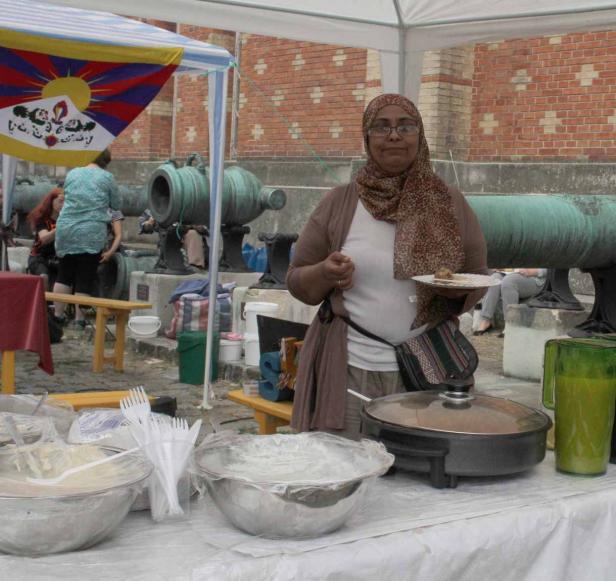 Eine Frau mit Kopftuch verkauft Essen an einem Stand mit tibetischer Flagge im Hintergrund.