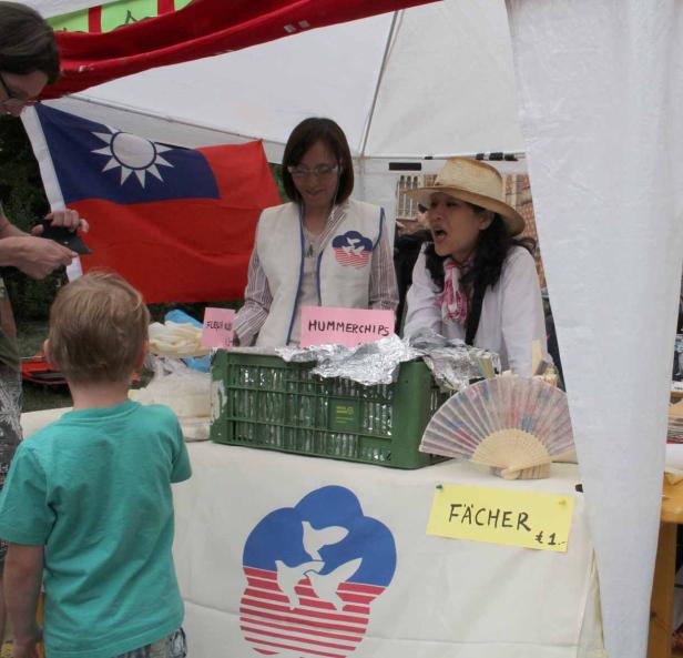 Zwei Frauen verkaufen an einem Stand Hummerschips und Fächer vor einer Taiwan-Flagge.