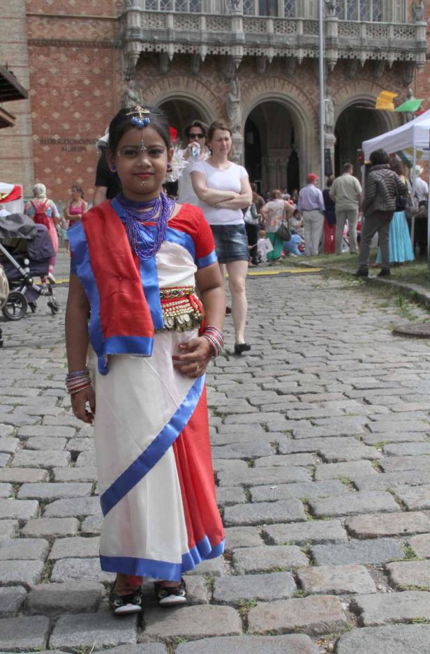 Ein junges Mädchen in traditioneller indischer Kleidung steht auf einem gepflasterten Platz.