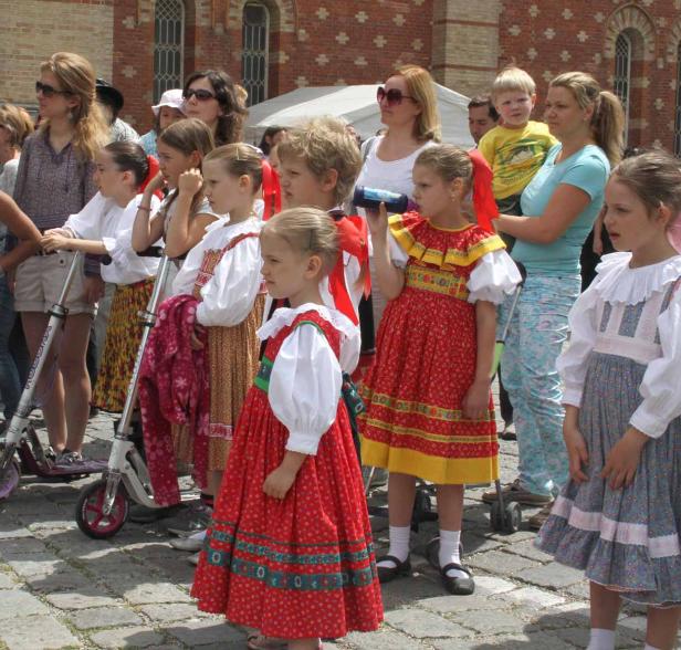 Eine Gruppe von Kindern in Trachten steht auf einem gepflasterten Platz.