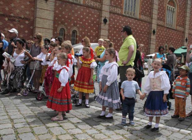 Eine Gruppe von Kindern in Trachten steht auf einem gepflasterten Platz.