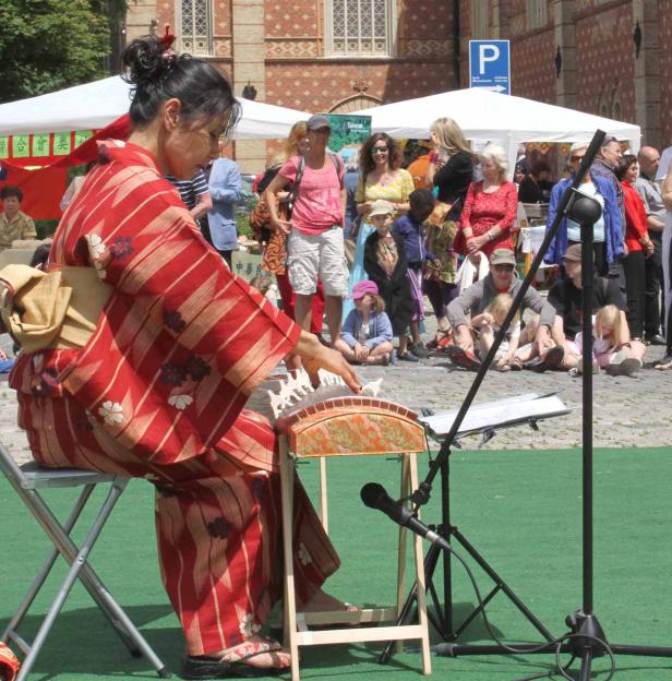 Eine Frau im Kimono spielt ein traditionelles japanisches Musikinstrument vor Publikum.