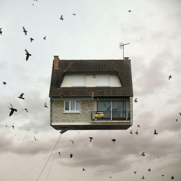 Ein Haus schwebt inmitten einer Wolke von Vögeln, ein „Zu Verkaufen“-Schild am Balkon.