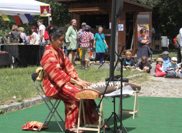 Eine Frau im Kimono spielt ein traditionelles japanisches Musikinstrument im Freien.