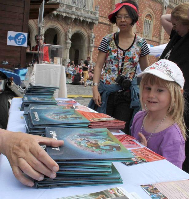 Ein junges Mädchen betrachtet Bücher auf einem Tisch im Freien.