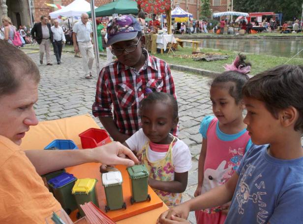 Ein Mann erklärt Kindern auf einem Markt das Mülltrennsystem.