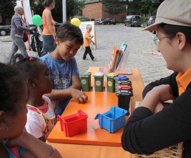 Kinder lernen spielerisch etwas über Mülltrennung an einem Stand im Freien.