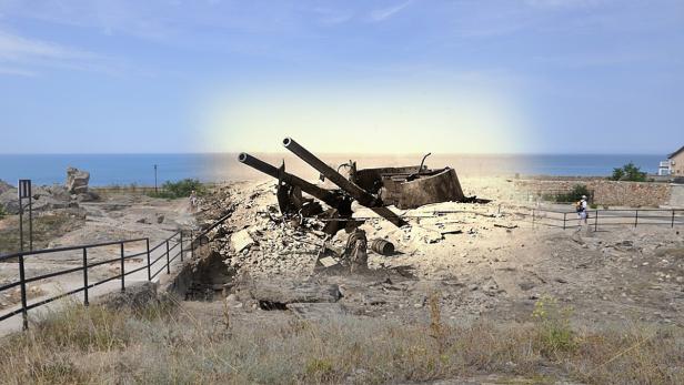 Eine zerstörte Geschützstellung mit zwei Kanonenrohren vor dem Hintergrund des Meeres.
