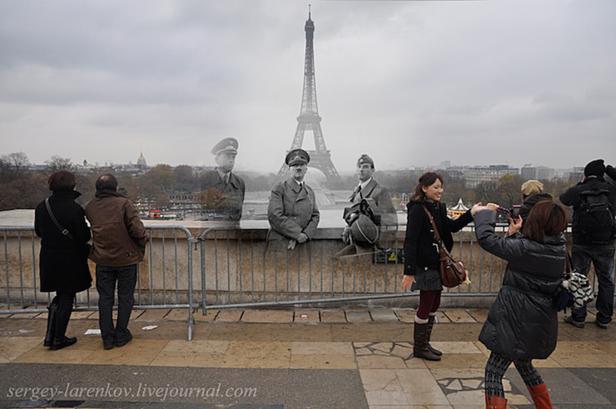 Besucher in Paris posieren vor einer Fotomontage mit Hitler und Wehrmachtsoffizieren vor dem Eiffelturm.