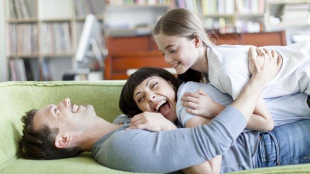 Eine Familie hat Spaß und lacht zusammen auf einem grünen Sofa.