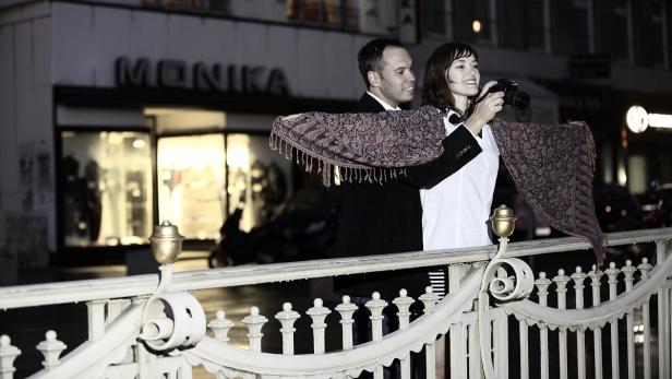 Ein Paar posiert mit einem Schal für ein Foto vor einem Geschäft namens „Monika“.