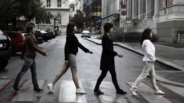 Vier Frauen überqueren einen Zebrastreifen in einer städtischen Umgebung.