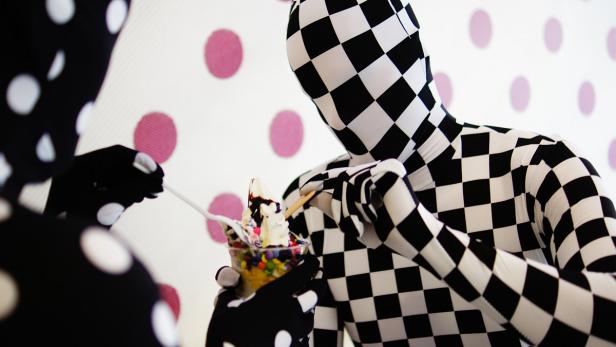 Zwei Personen in schwarz-weiß gemusterten Ganzkörperanzügen essen Eis mit bunten Streuseln.