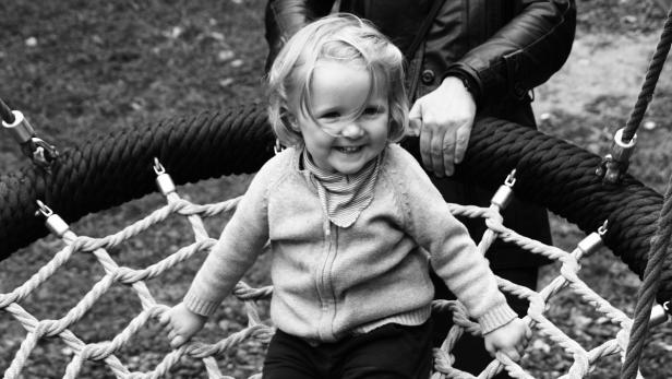 Ein lächelndes kleines Kind sitzt auf einer Nestschaukel.