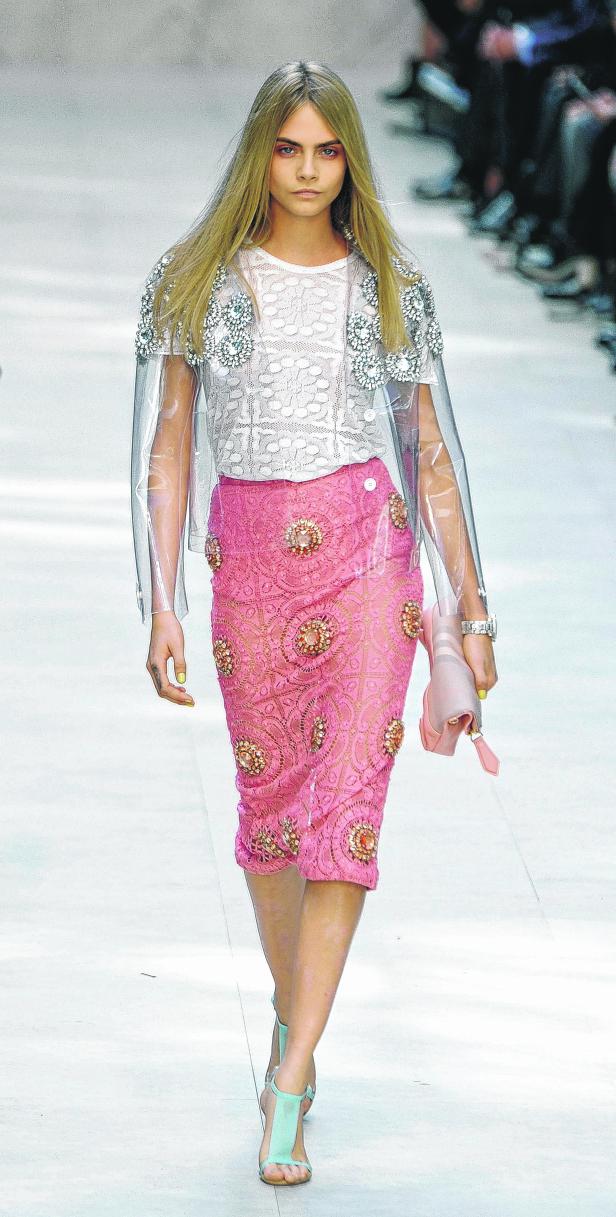 Cara Delevingne läuft in einem transparenten Cape und einem rosa Rock über einen Laufsteg.