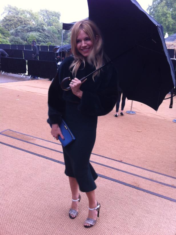 Sienna Miller steht mit einem Regenschirm auf einem Laufsteg.