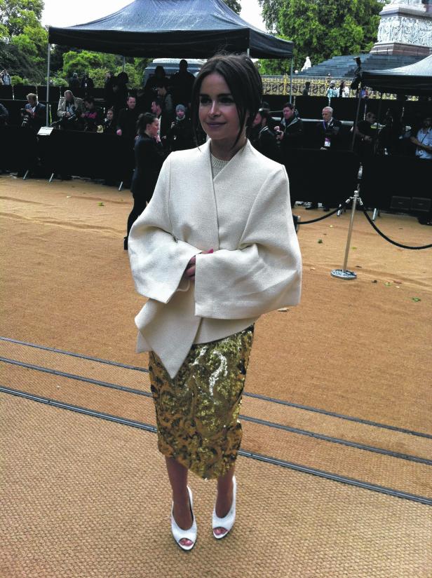 Eine Frau in einem weißen Blazer und einem goldenen Paillettenrock posiert für ein Foto.