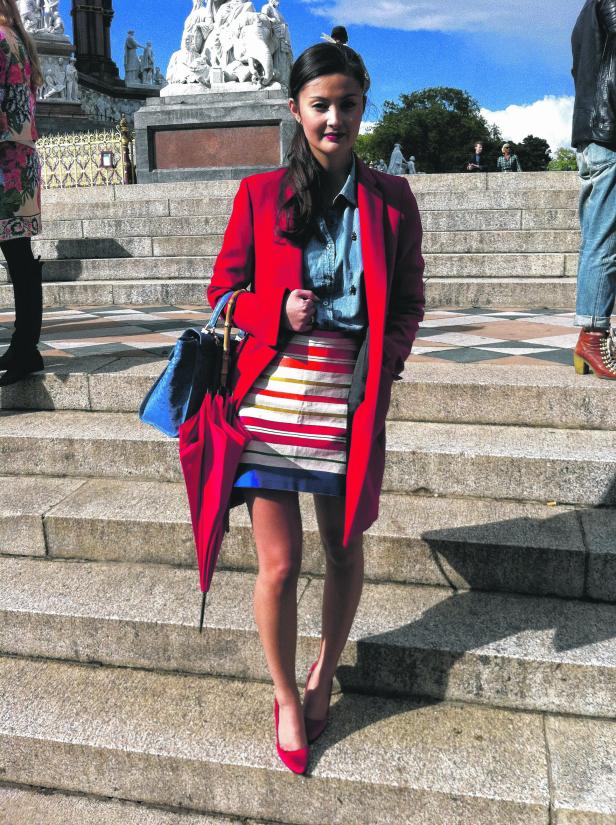 Eine Frau in einem roten Mantel steht auf einer Steintreppe.