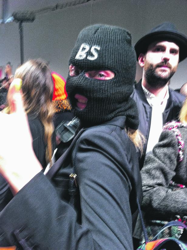 Eine Person mit Sturmhaube mit der Aufschrift „BS“ steht in einer Menschenmenge.