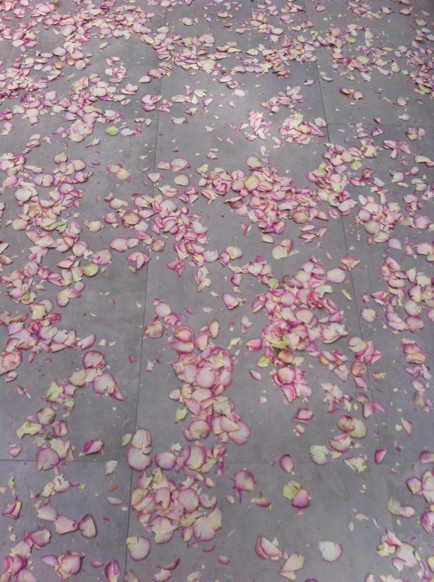 Rosa Blütenblätter liegen verstreut auf einem grauen Fliesenboden.