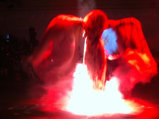 Eine Person mit Flügeln steht in rotem Licht und Nebel.