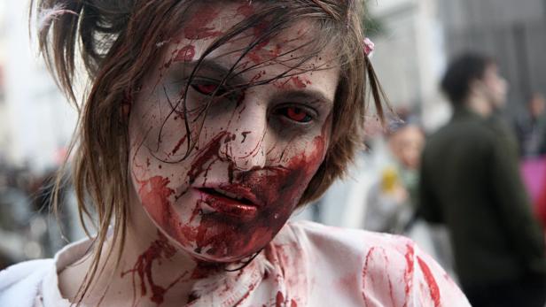Eine Frau mit roter Kontaktlinse und blutverschmiertem Gesicht als Zombie geschminkt.