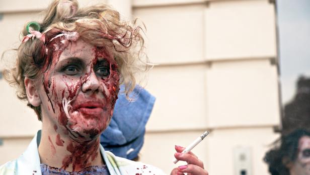 Eine Frau mit blutverschmiertem Gesicht und Lockenwicklern raucht eine Zigarette.