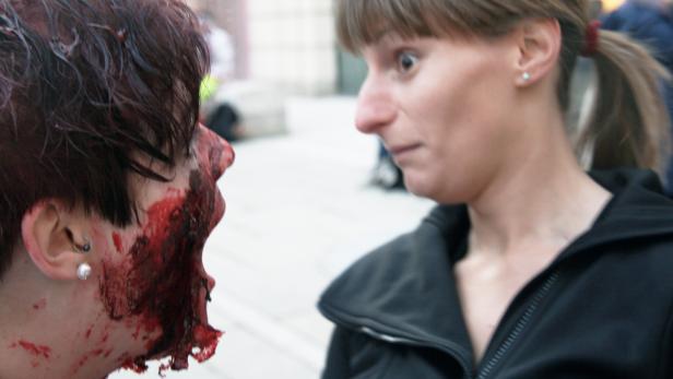 Eine Frau blickt entsetzt auf eine andere Frau mit blutverschmiertem Gesicht.