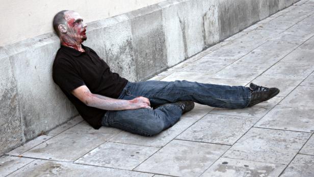 Ein Mann mit blutverschmiertem Gesicht lehnt an einer Wand.