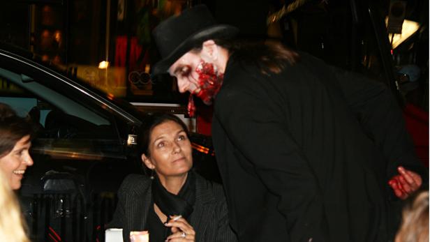 Eine Frau raucht, während ein Mann mit Zombie-Make-up über sie gebeugt steht.