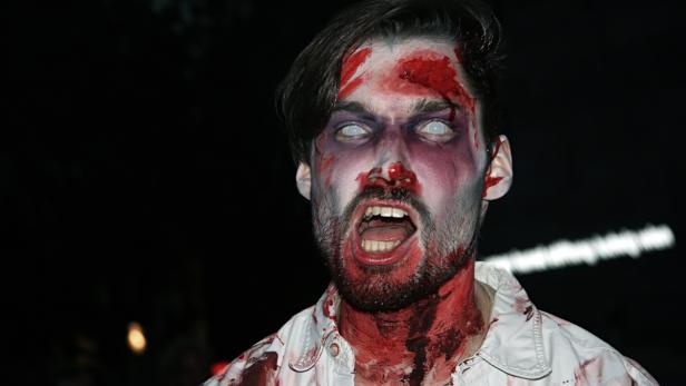 Ein Mann mit blutigem Zombie-Make-up und weißen Kontaktlinsen schreit.