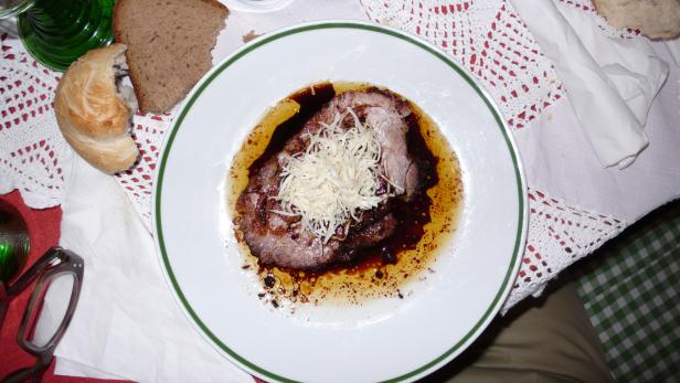 Ein Teller mit Fleisch, bedeckt mit Käse und Sauce, steht auf einem Tisch.