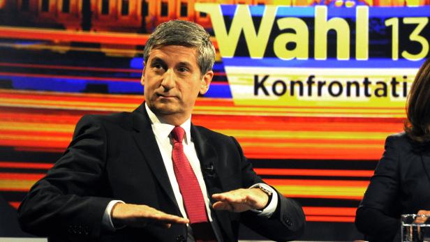 Ein Mann im Anzug gestikuliert vor dem Hintergrund einer Wahlkampfveranstaltung.