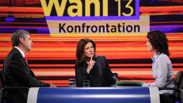 Drei Personen sitzen an einem Tisch vor dem Hintergrund einer „Wahl 13“-Konfrontation.
