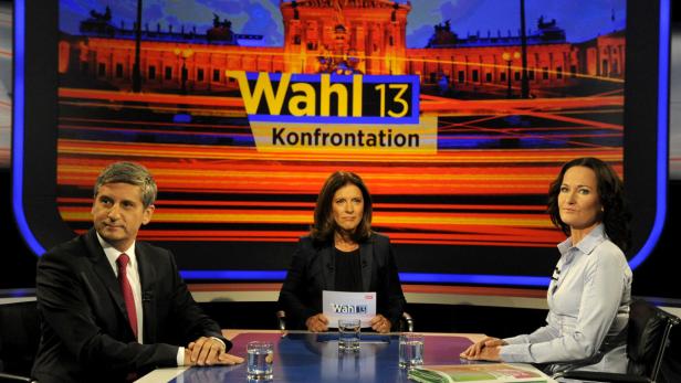 Drei Personen sitzen an einem Tisch vor dem Hintergrund einer „Wahl 13“-Konfrontation.