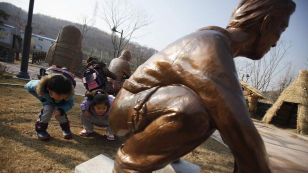 Kinder beobachten eine Statue eines Mannes in einer Parkanlage.
