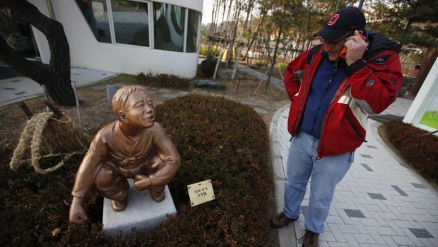 Ein Mann telefoniert neben einer Bronzestatue eines hockenden Jungen.
