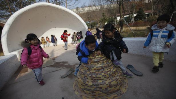 Eine Gruppe von Kindern spielt auf einem Spielplatz mit einer halbrunden Struktur.