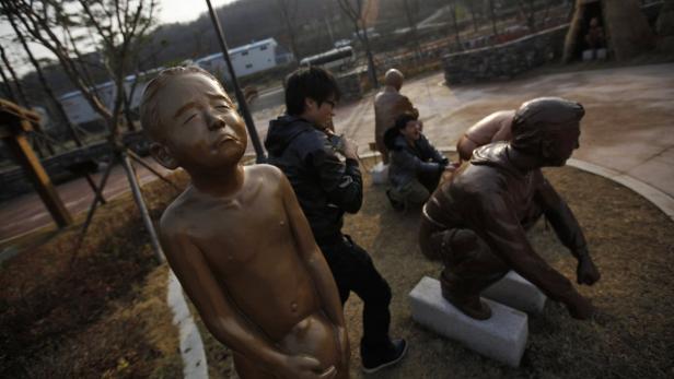 Ein Park mit skulpturalen Darstellungen von Menschen beim Stuhlgang, fotografiert von Touristen.