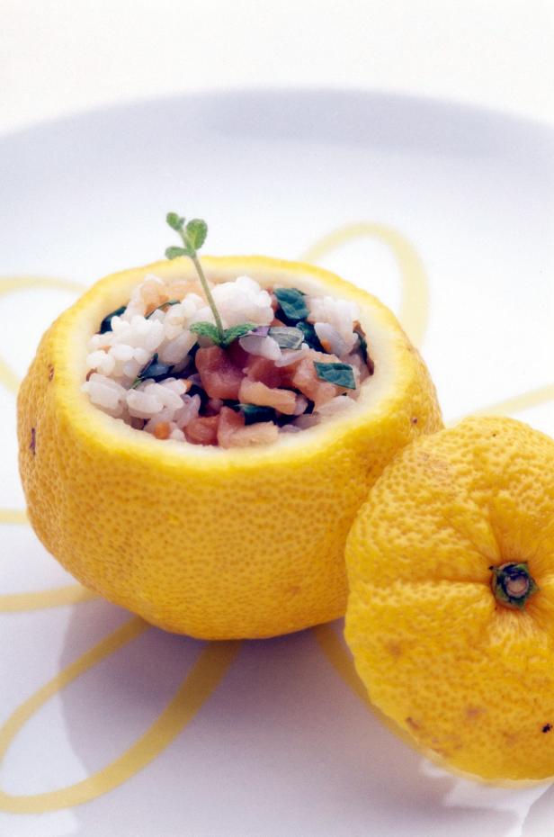 Eine halbe Zitrone gefüllt mit Reis, Fisch und Kräutern auf einem Teller.