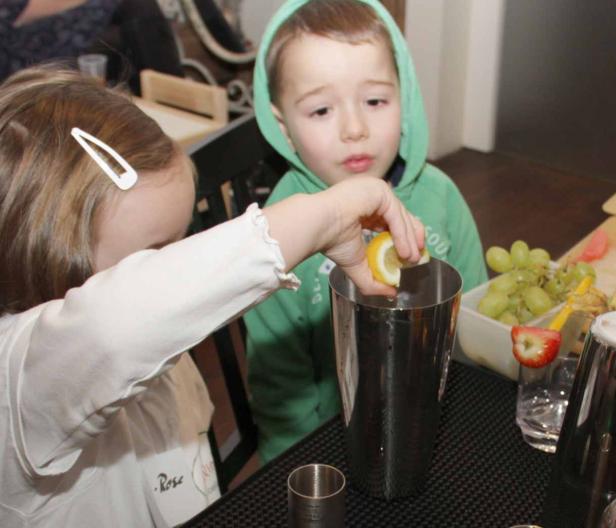 Ein Mädchen presst eine Zitrone in einen Cocktailshaker, während ein Junge zusieht.