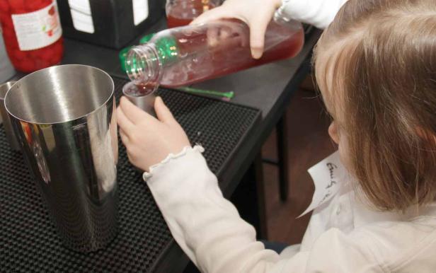 Ein Mädchen gießt eine rote Flüssigkeit aus einer Flasche in einen Messbecher.
