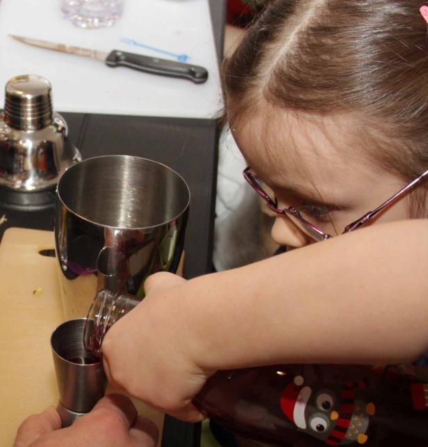 Ein Mädchen mit Brille gießt eine rote Flüssigkeit in einen Messbecher.