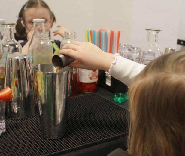 Ein Kind gießt eine Flüssigkeit mit einem Messbecher in einen Cocktailshaker.