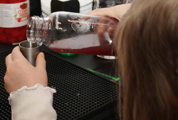 Ein Mädchen gießt eine rote Flüssigkeit aus einem Glas in einen Messbecher.