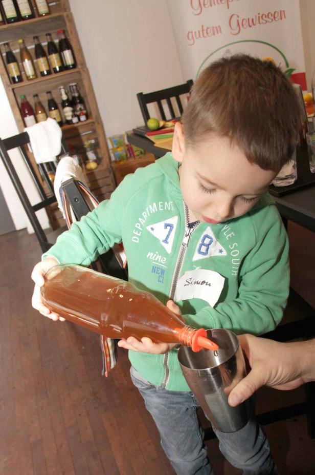 Ein Junge namens Simon gießt Saft aus einer Flasche in einen Shaker.