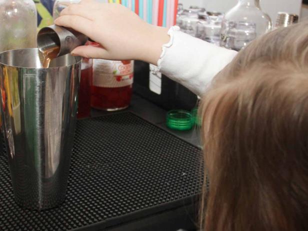 Ein Kind gießt eine braune Flüssigkeit in einen Cocktailshaker.