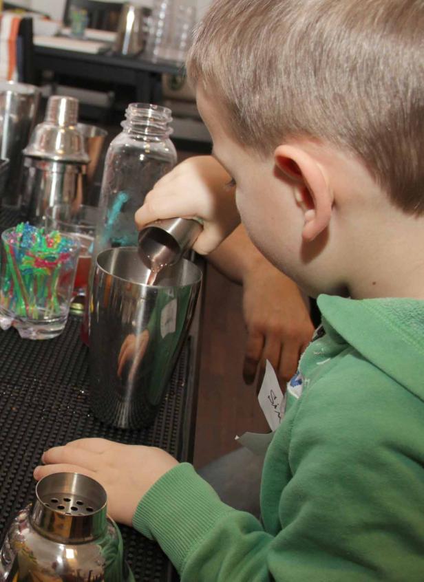 Ein Junge gießt mit einem Messbecher Flüssigkeit in einen Cocktailshaker.