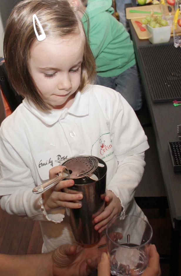 Ein kleines Mädchen mit Namensschild mixt einen Drink in einem Shaker.