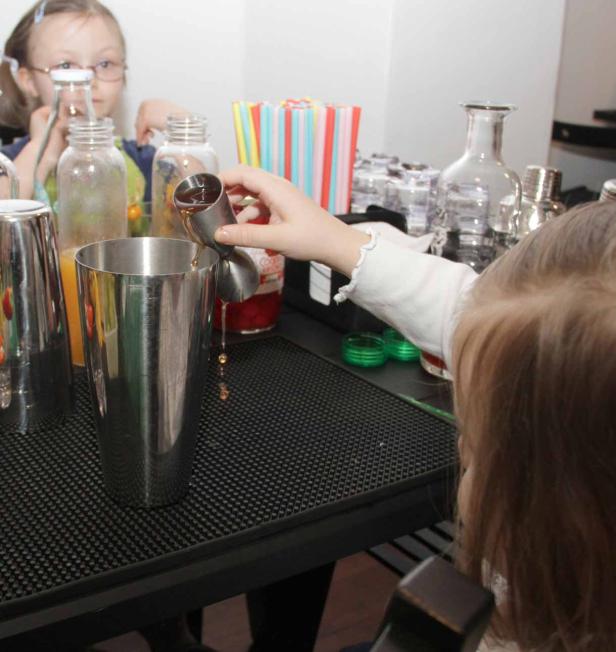 Ein Kind gießt mit einem Messbecher Flüssigkeit in einen Cocktailshaker.